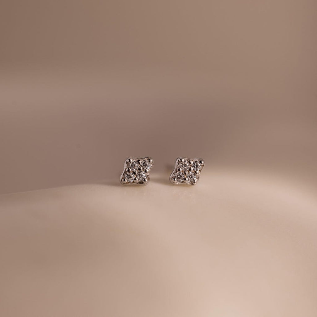 Pair of silver kite-shaped earrings with embedded stones on a beige background