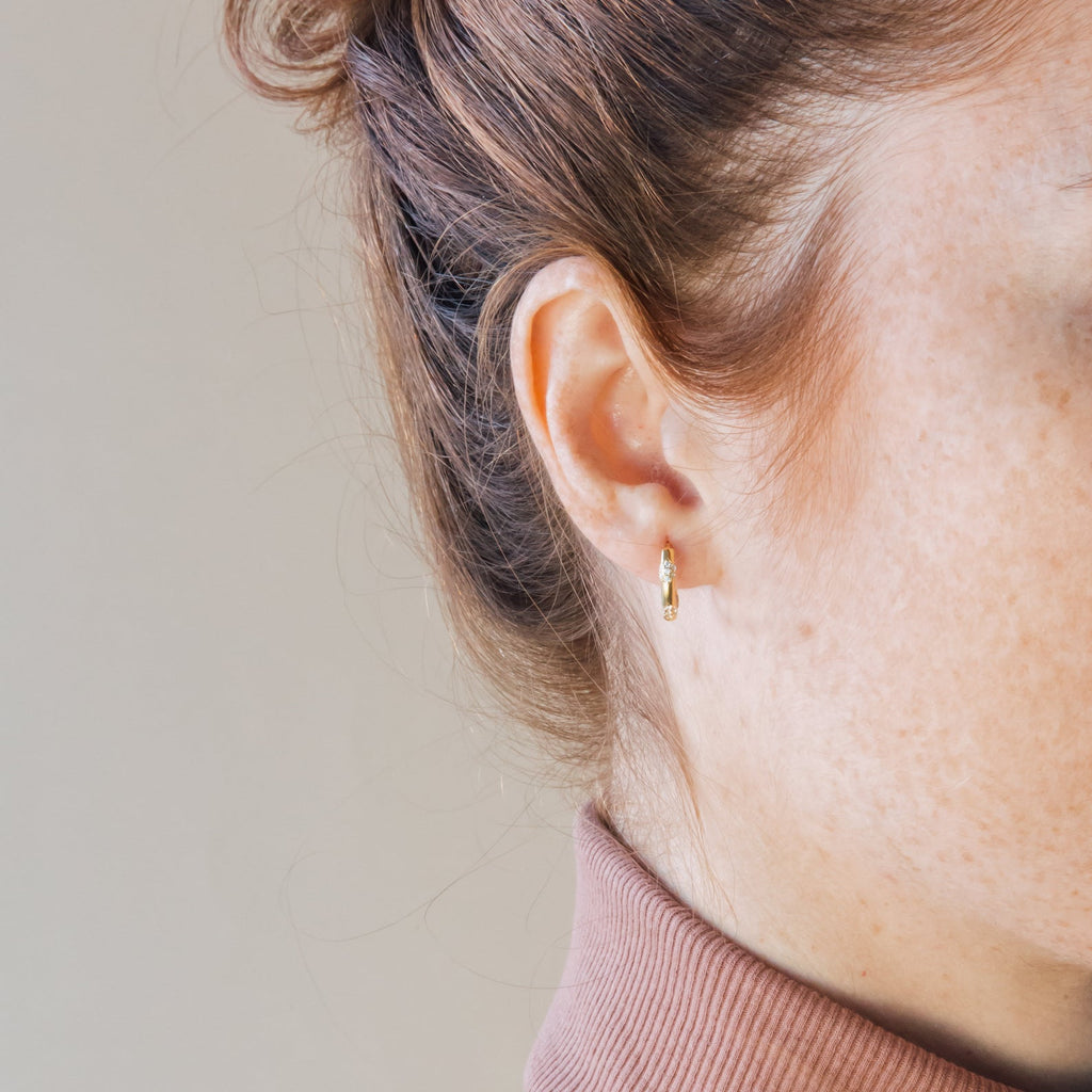 Close-up of a model wearing a gold diamond hoop earring with a neutral background