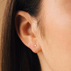 Close-up of a person's ear wearing Tiny Cross Studs in 18K Gold—dainty earrings that add a subtle, elegant touch.