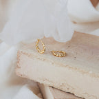 Naomi Twisted Hoops in 18K Gold displayed on light-colored stone slabs with a soft fabric background.