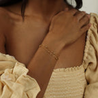 A woman wears the Duo Bead Chain Bracelet with a cream off-shoulder, textured dress featuring puffed sleeves.