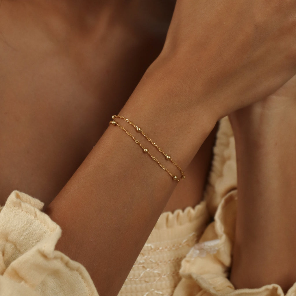 A close-up of a woman’s wrist wearing the Duo Bead Chain Bracelet, styled with a cream-colored blouse.