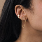 Close-up of a woman's ear adorned with two gold earrings from the Diamond Chain Earrings Set—one is a hoop, while the other is a delicate diamond chain earring connecting two piercings.