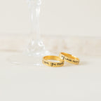 Two gold Handwriting Bands, engraved with "I love you more" and "my whole heart," rest by a wine glass base—ideal as a Christmas gift or personalized jewelry for someone special.
