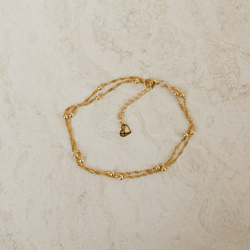 Gold anklet on a light beige textured surface