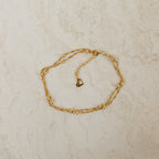 Gold anklet on a light beige textured surface