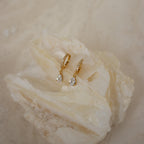 Diamond Drop Huggies in 18K Gold with teardrop gemstones shimmer on a textured, light surface—ideal for bringing elegance to semi-formal outfits.