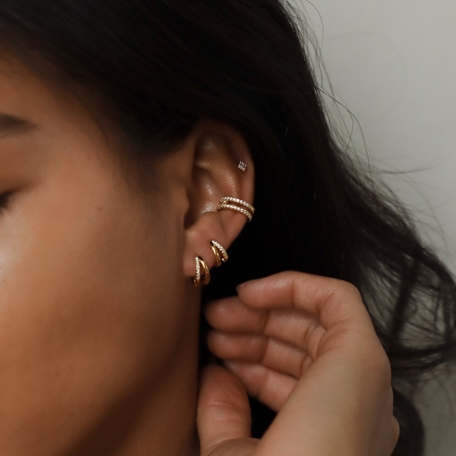 Multiple Amelia Duo Huggies styled along a model’s ear with additional gold and crystal cuffs.