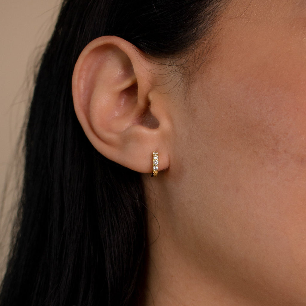 A close-up of an ear wearing a small gold Elise Gemstone Huggies Set with embedded stones, highlighting the elegant charm of artisan-made earrings.