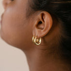 A close-up of a person's ear wearing two Paris Oval Hoops—elegant gold earrings that add timeless charm.