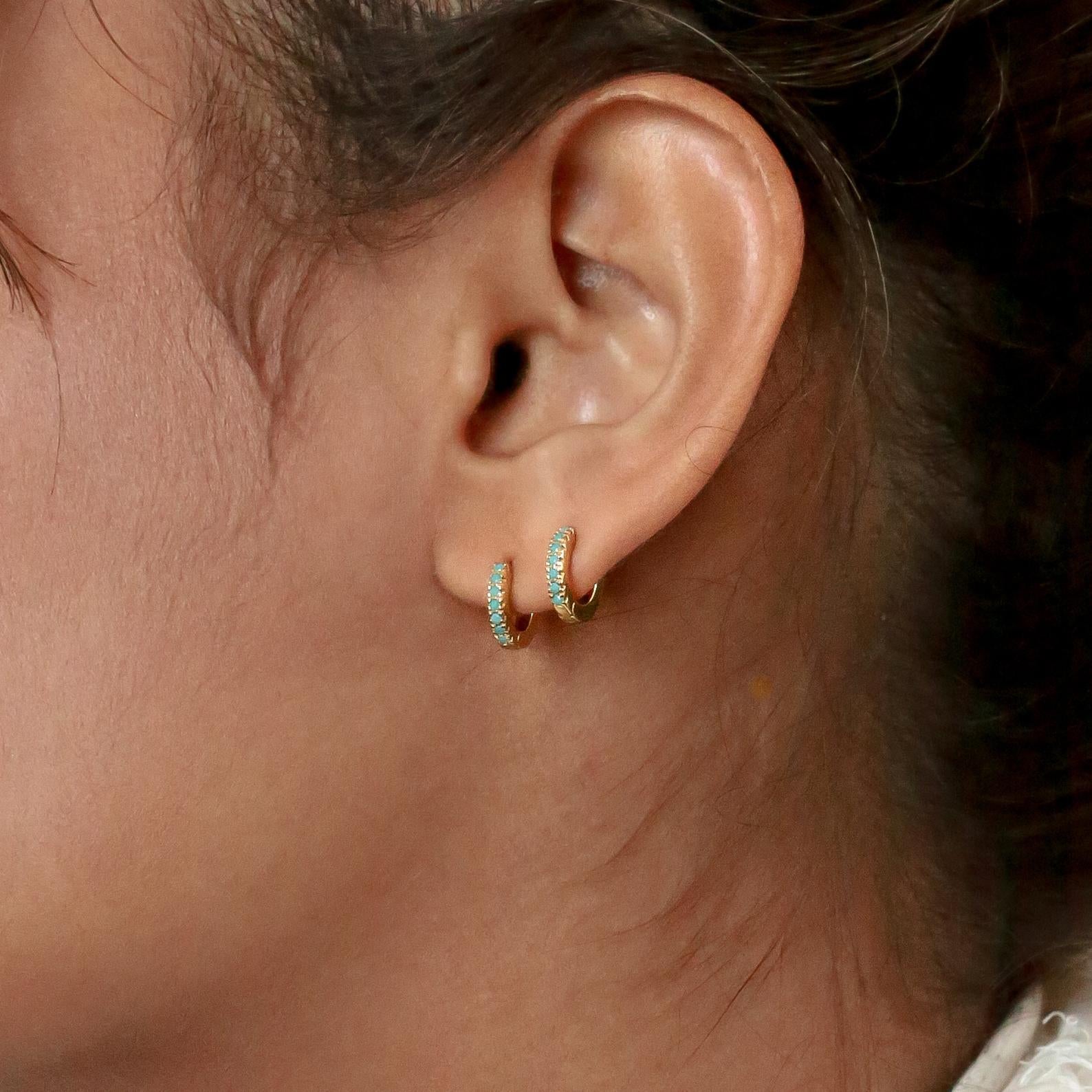 Close-up of a person's ear adorned with two small gold hoops featuring turquoise stones, highlighting the Boho Turquoise Earring Set for a touch of bohemian style.