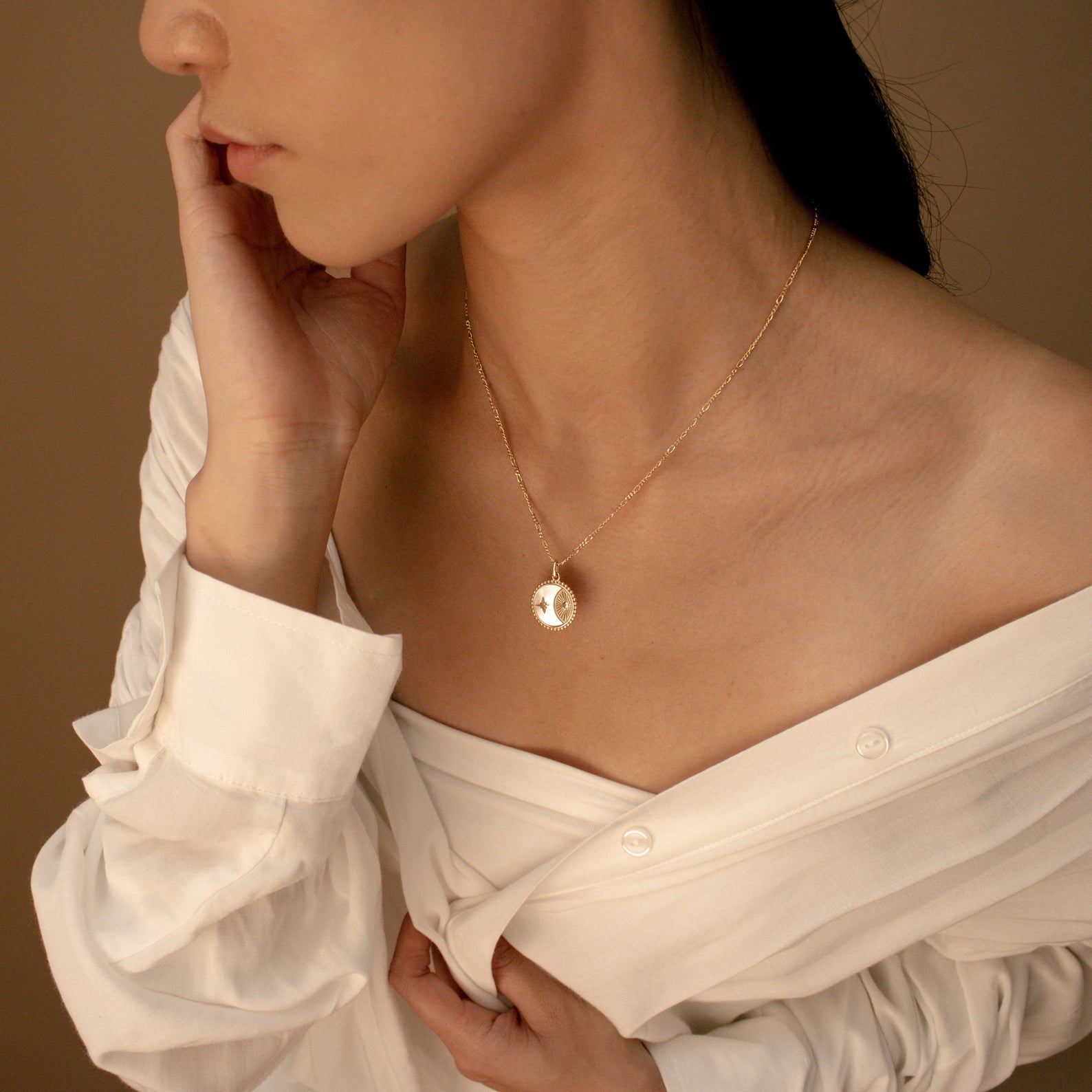 A woman in an off-shoulder white shirt wears the Gabi Coin Necklace, featuring a minimalist round pendant, set against a beige background.