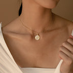 A woman wears the Gabi Coin Necklace, a minimal gold accessory, paired with a white top and shown from the shoulders up.