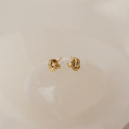 Love Knot Studs in Sterling Silver are shown on a smooth, light-colored stone background—these symbolic earrings make a perfect unity gift.