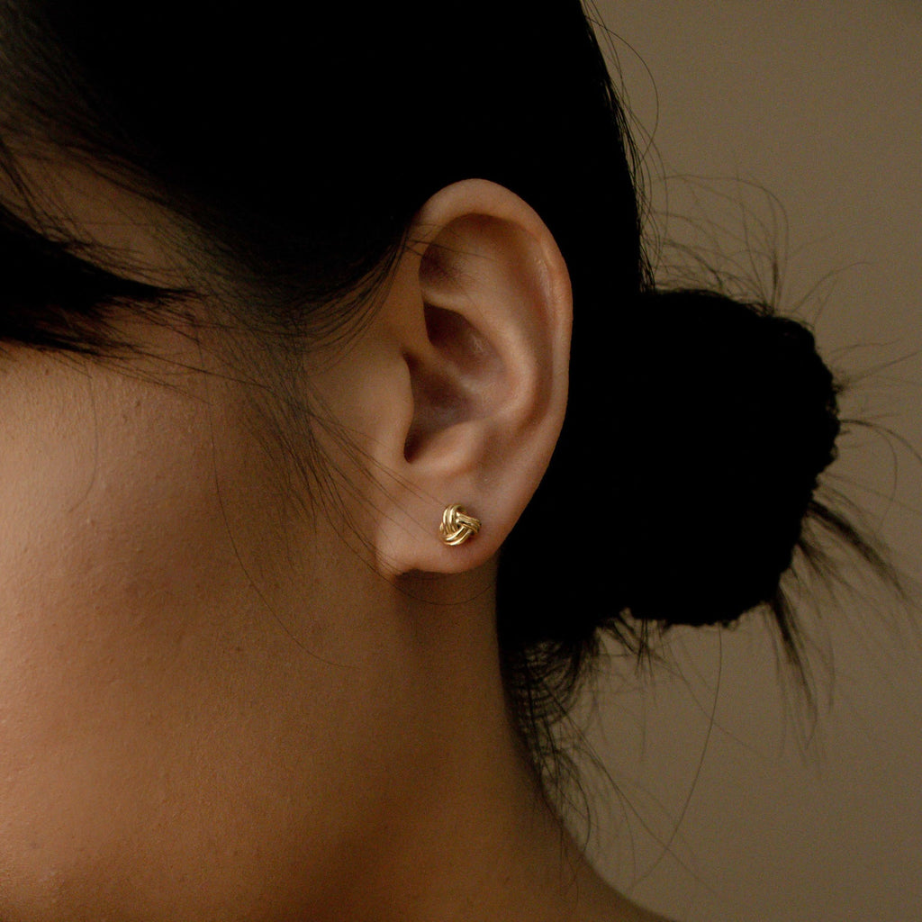Close-up of a woman's ear wearing Love Knot Studs in Sterling Silver, with dark hair in a low bun—symbolic jewelry perfect as a unity gift.