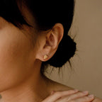 Close-up of a woman with dark hair in a bun wearing Love Knot Studs in 18K Gold—symbolic earrings that make a thoughtful gift—her hand resting gently near her neck.