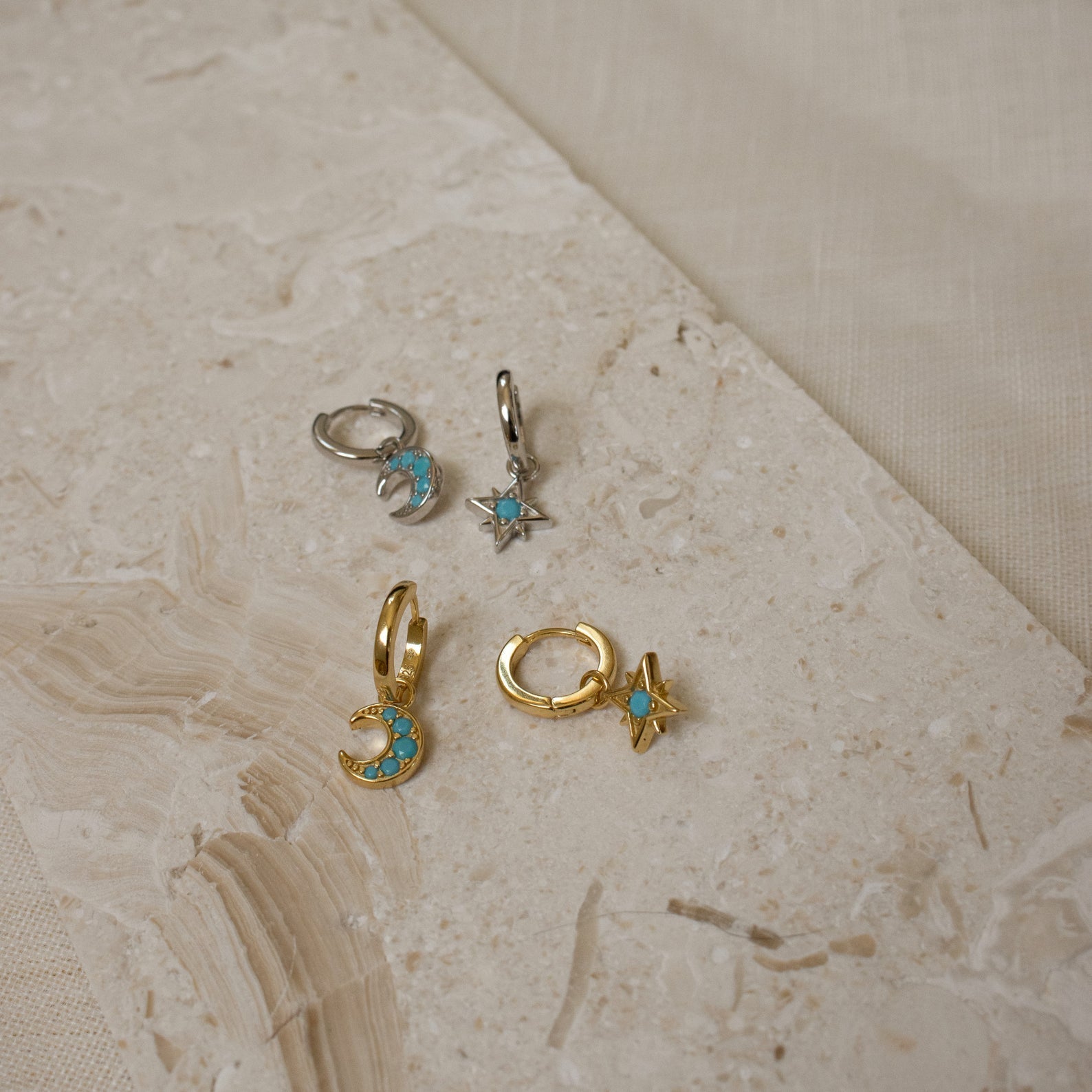 The Boho Turquoise Earring Set features four small gold and silver earrings with moon and star designs and turquoise stones, displayed on a textured beige surface—perfect for lovers of turquoise jewelry.