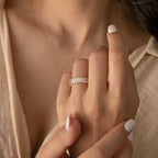A hand with white nail polish wears the Colette Eternity Ring, a gold band adorned with multiple rectangular baguette diamonds for a look of subtle opulence.