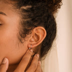 Jady Wire Diamond Hoop earring in 18K gold worn on ear with hand touching earlobe.