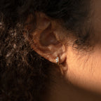 Close-up of a person's ear wearing the Giana Marquise Huggies—small gold hoops with a clear gemstone—shining in sunlight and highlighting the elegance of these subtle earrings.