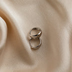 Two Olivia Hoops in Sterling Silver rest on smooth, beige satin fabric with soft folds, creating a chic and elegant scene.