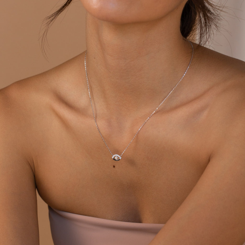 A woman in a strapless top wears the Amaryllis Pave Evil Eye Necklace, featuring a delicate diamond evil eye pendant for protection.