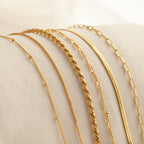 Six gold chain necklaces in various link styles, displayed on a white cushioned surface, pair stylishly with Must-Have Bracelet Chains for a chic, coordinated look.