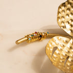 Gold rings with colorful gemstones stacked on a golden branch beside a decorative golden leaf, perfect for pairing with personalized jewelry or Athena Birthstone Huggies.