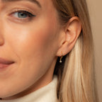 Close-up of a woman with blonde hair and a soft smile wearing Molly Pearl Huggies—a gold huggie hoop earring featuring a delicate dangling pearl.