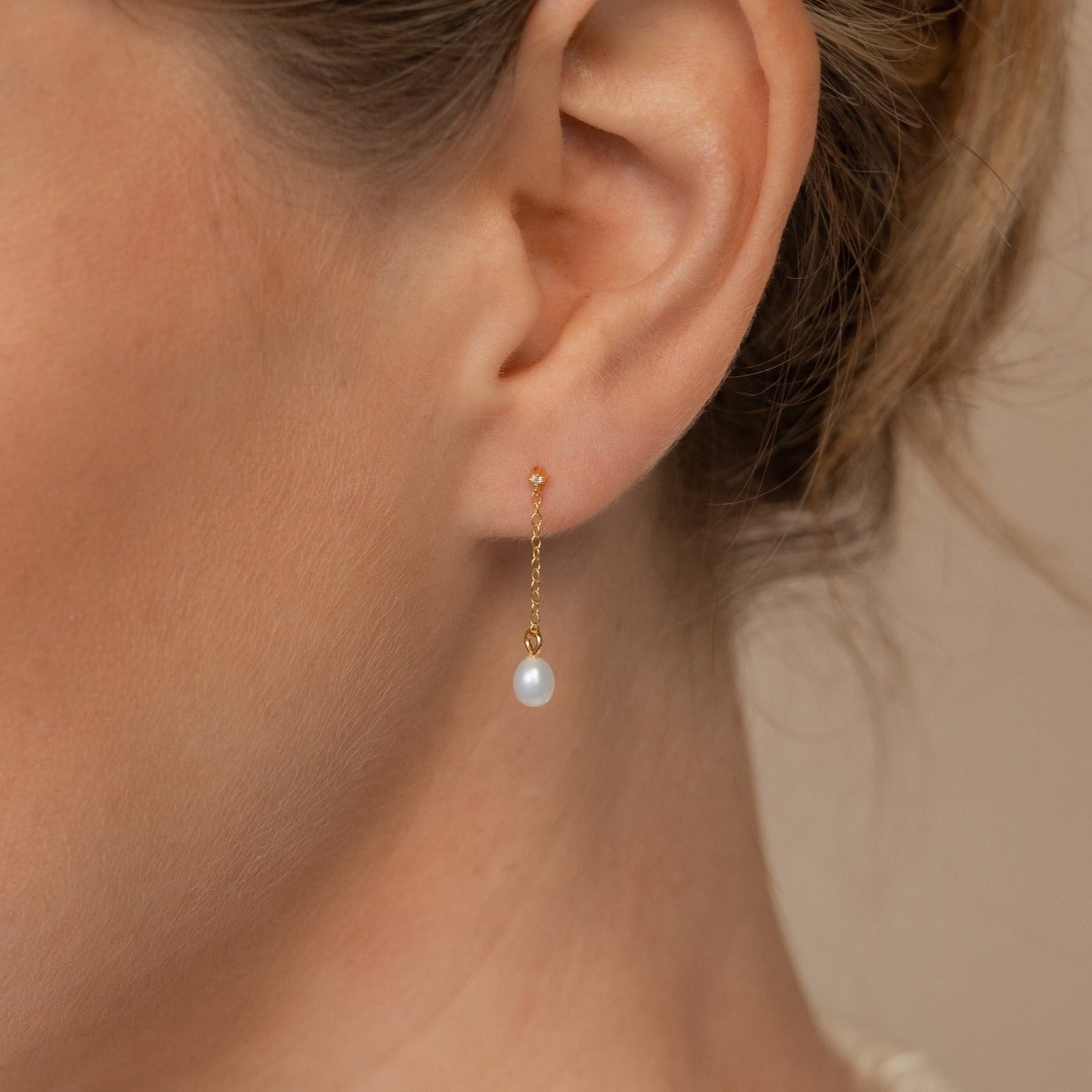 Close-up of a woman's ear adorned with the Isha Pearl Drop Earrings, which showcase a delicate gold chain and a dainty white pearl charm.