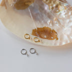 Two pairs of Molly Pearl Huggies, one gold and one silver, displayed on a large iridescent seashell.