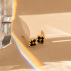 Onyx Diamond Earrings Set featuring small black stones on a beige surface, beside a prism casting a rainbow—ideal for those who appreciate the delicate charm of these elegant earrings.
