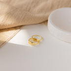 The Old English Signet Ring, a gold custom engraved piece with “11:11,” rests beside another gold band on a white surface and soft beige fabric—ideal for fans of personalized jewelry.