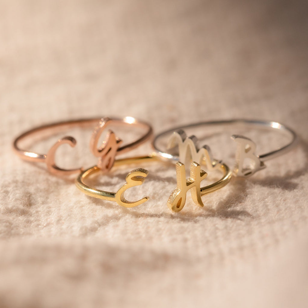 The Nella Duo Initial Ring—engraved with custom initials—rests on textured beige fabric, showcasing a personalized jewelry piece and a thoughtful anniversary gift.