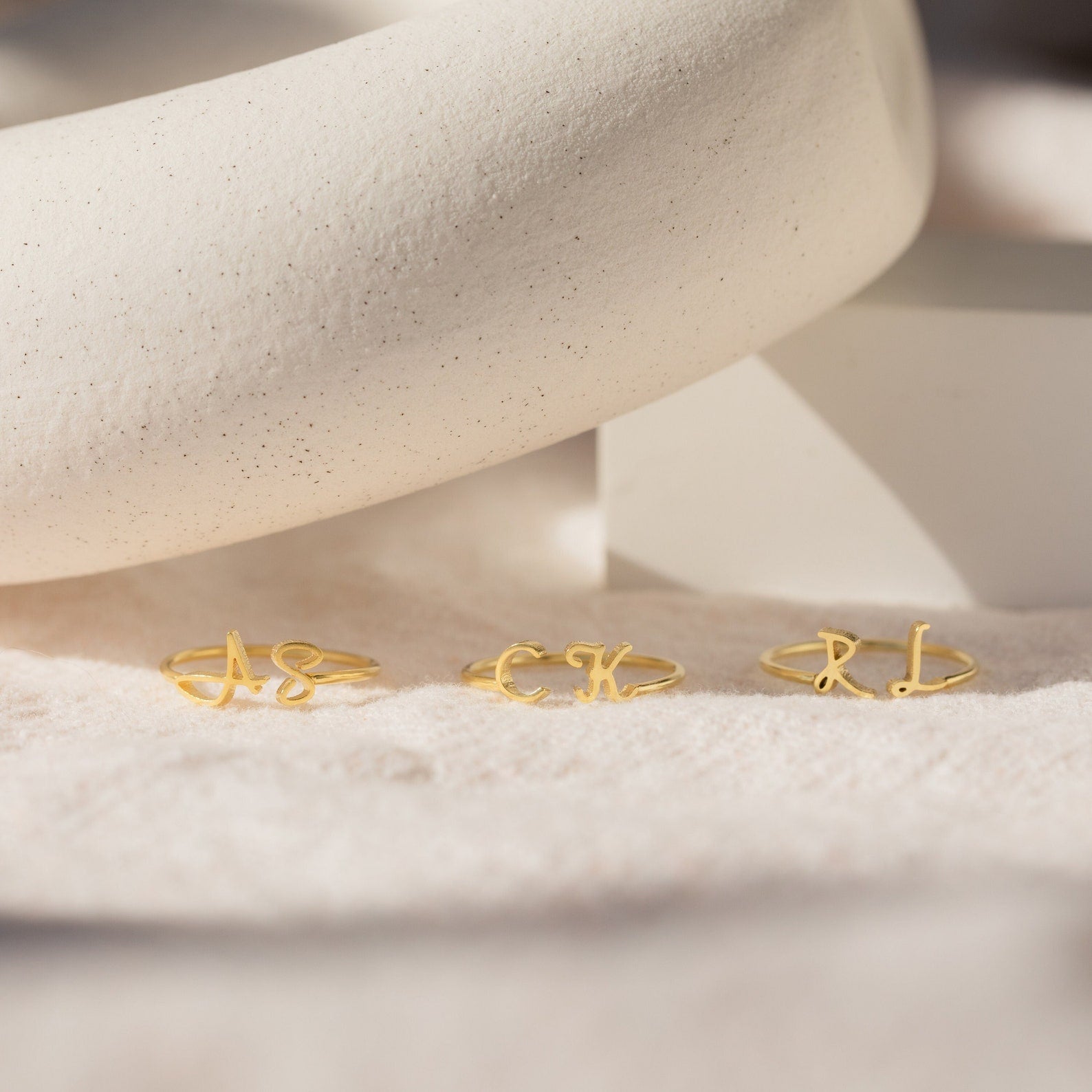 The Dainty Duo Initial Ring showcases elegant gold bands featuring your chosen letters, beautifully displayed on a soft, neutral fabric—ideal as a personalized gift or anniversary keepsake.