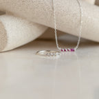An Initial Morse Code Ring in silver with four small diamonds and a delicate pink stone necklace are displayed on a light textured surface, highlighting the personalized elegance of this jewelry.