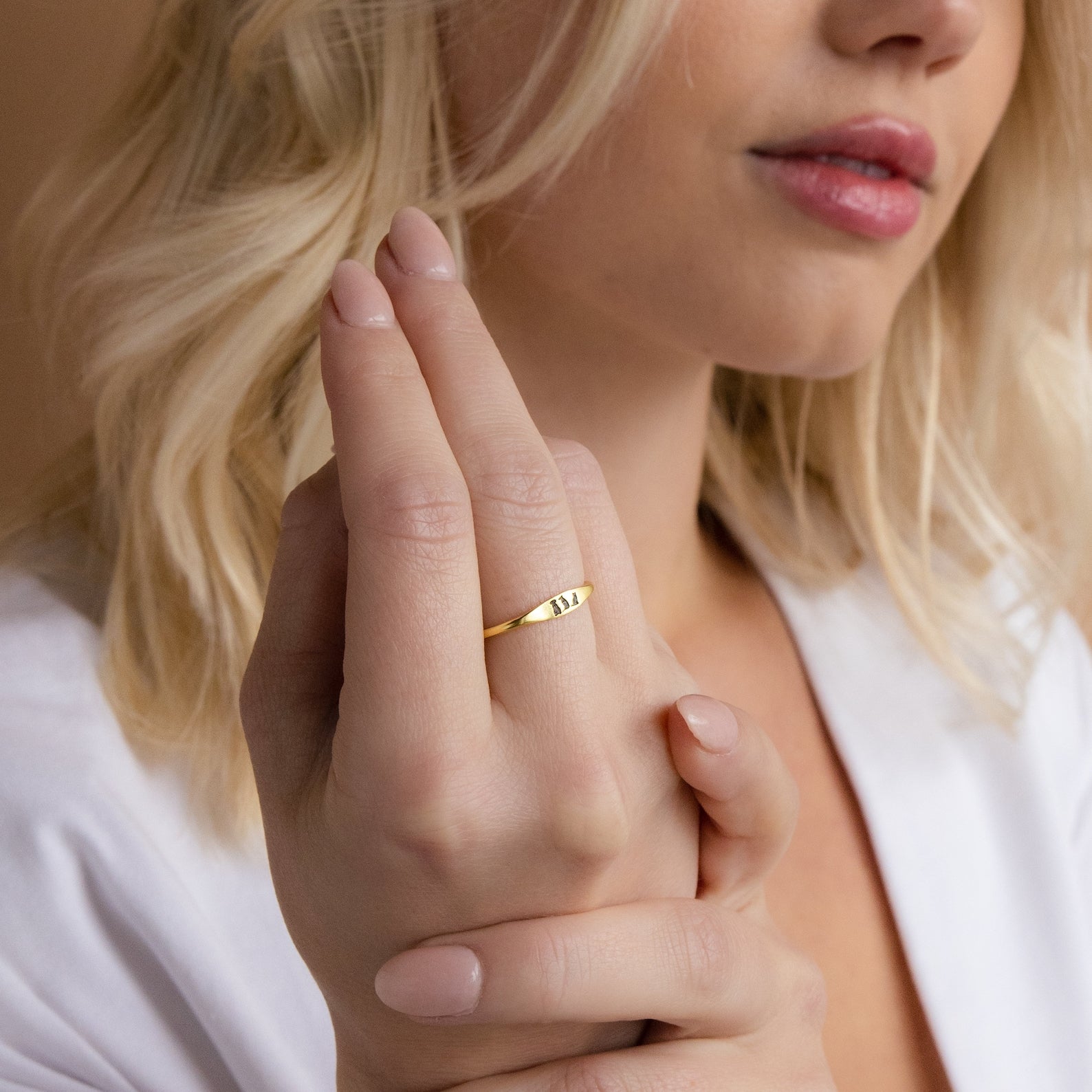 A blonde-haired woman wears the Skinny Pet Ring—a dainty, personalized piece engraved with her pet's name—on her finger, holding her hand near her face.