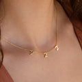 The Old English Spaced Number Necklace features three number 2 charms in a vintage style, elegantly worn for a personalized look—an eye-catching example of unique number jewelry.