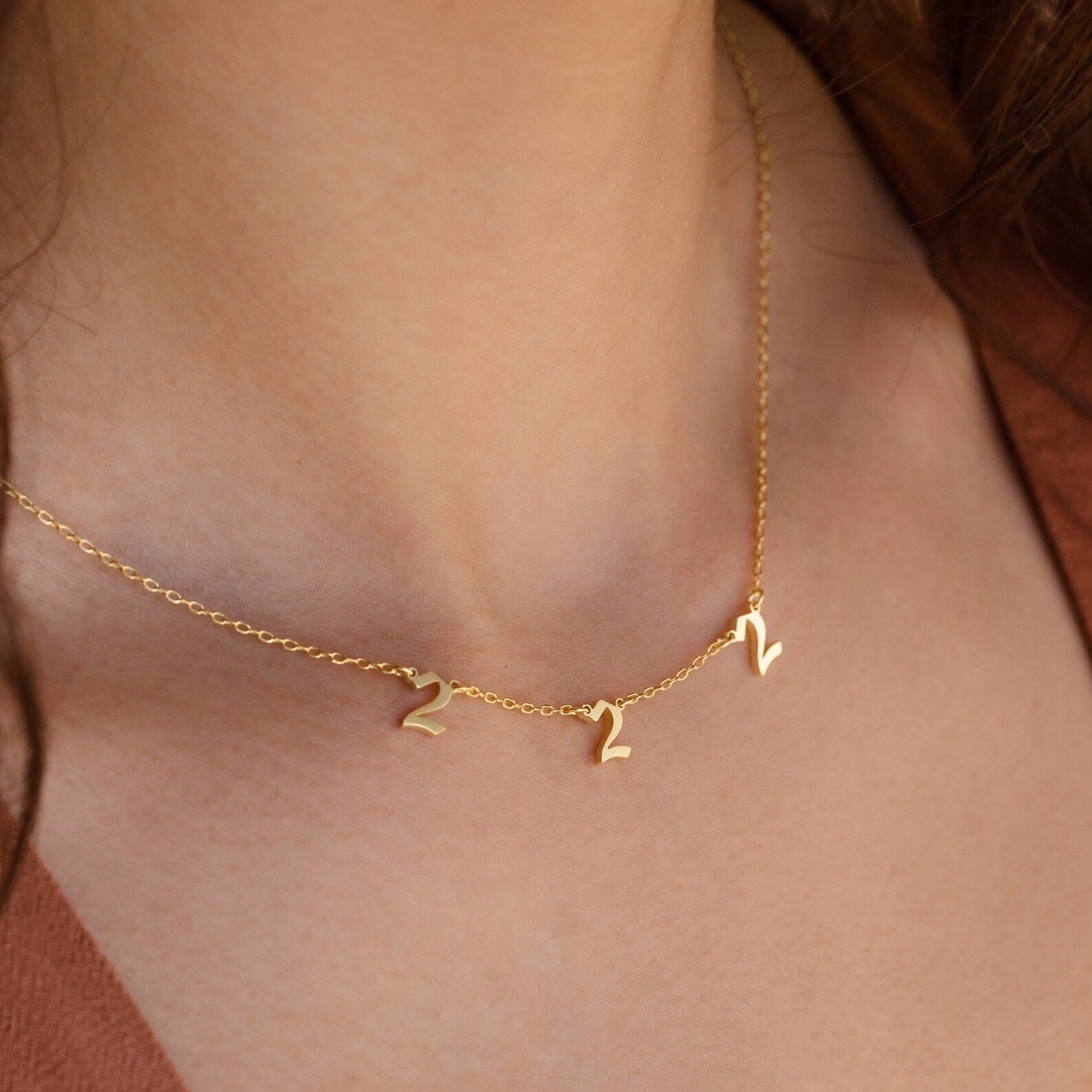 The Old English Spaced Number Necklace features three number 2 charms in a vintage style, elegantly worn for a personalized look—an eye-catching example of unique number jewelry.