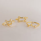 Three delicate gold Constellation Rings with small, sparkling flower-shaped designs evoke celestial jewelry, beautifully displayed on a light surface.