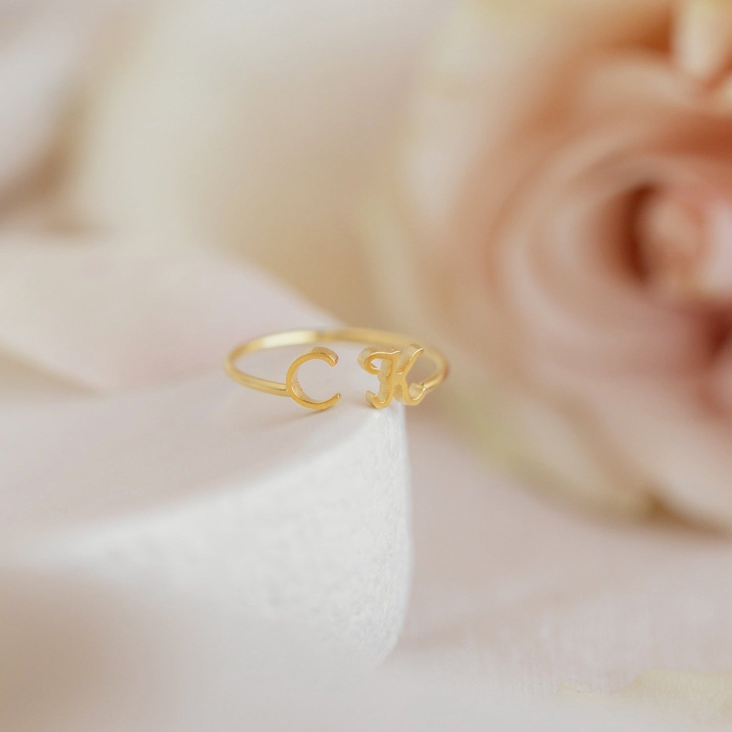 The Dainty Duo Initial Ring with C and K, framed by soft pink and cream flowers, makes a perfect personalized gift for anniversaries.