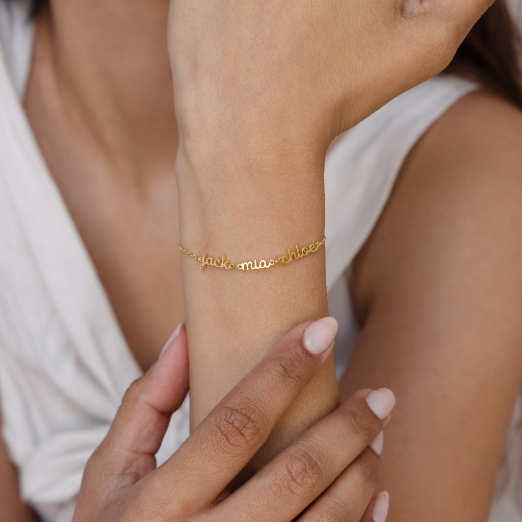 A woman’s wrist adorned with a Petite Tiny Multiple Name Bracelet, her hand gently touching her arm—this minimal jewelry piece adds a personalized touch to any look.