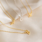 The Grace Dainty Initial Necklace in gold and silver is elegantly displayed on cream-colored fabric, making it a perfect addition to your personalized necklace collection.