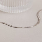 A minimalist necklace, this Men's Snake Chain Necklace is displayed on a light surface beside a textured glass object.