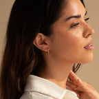 Woman with long dark hair looks to the side in soft, warm lighting, wearing Halo Opal Hoops—elegant gold huggie earrings.