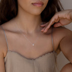 Woman wearing a beige spaghetti strap top and the Stylish Dainty Initial Necklace with an “R” pendant, her hand near her face.