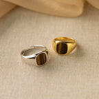 The Tigers Eye Signet Ring, featuring a striking tiger’s eye stone and classic signet design, is showcased on a beige textured fabric background.