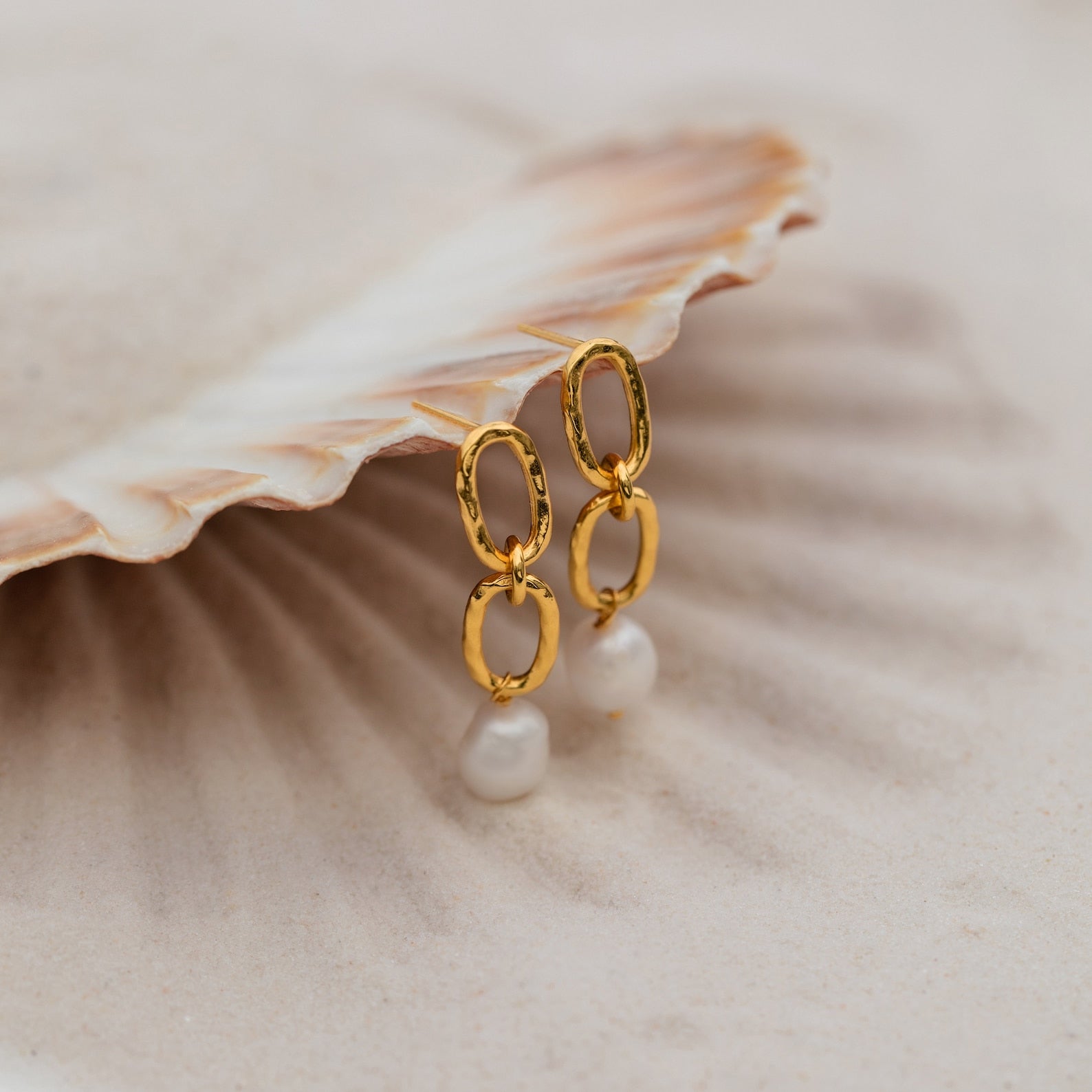 Pearl Drop Link Studs rest on a textured seashell background, creating elegant statement earrings that bring a touch of coastal charm.