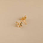 Seagrass Peridot Marquise Studs: Gold stud earrings with marquise and round-cut peridot stones add elegant sparkle against a beige backdrop.