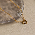Delicate gold necklace with a simple open circle pendant resting on a fine chain, styled on a textured neutral background.
